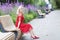 A young woman sits on a bench in a blooming park. Smiling beautiful blonde in a bright red dress