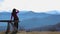 Young woman sits on bench outside and look at pictorial landscape with mountains