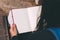 Young woman sits on bench in park with blank notebook and pen on her hands.