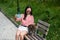 Young woman sits on a bench with a tabby cat and takes a selfie on a smartphone outdoors.