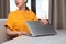 A young woman sits at a desk with headphones on, turns to the side, covering her laptop. A window in the background. The concept