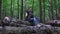 A young woman sits in the forest on logs, network loss on the phone. The girl takes pictures of nature on the camera of