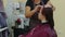 Young woman sits during hair care procedure in salon. Unrecognizable person wipes forehead with cotton pad of client