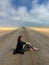 Young woman sits on highway in desert. Girl on center of the road, barefoot.