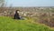 A young woman sits on a hill and looks down on the house