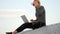 Young woman sits with laptop and listening music on headphones on the rooftop.