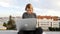 Young woman sits with laptop and listening music on headphones on the rooftop.