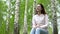 A young woman sits in nature with headphones in her ears. A girl sits on a stump in a birch forest and listens to music.