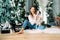 Young woman sits near Christmas tree and holds dalmatian puppy in her hands