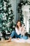 Young woman sits near Christmas tree and holds dalmatian puppy in her hands