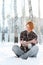 Young woman sits at snow in winter forest