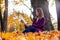 Young woman sits under a tree and reads a paper book.