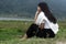 Young woman sitting alone on the ground with lake view background. Daydreaming concept.