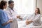 Young woman sitting on bed and looking at confident doctor pointing at paper