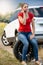 Young woman sitting on car spare wheel at her broken transport and calling service