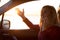 Young woman sitting in car and talking on the phone during sunset on the waterfront.