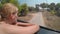 Young woman sitting in a car traveling along countryside road on sunny day vacation enjoying landscape -