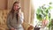 Young woman sitting on the couch , talking on the phone . In the background green flowers out of focus . Beautiful