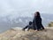 Young woman sitting on edge of cliff in foggy and cloudy weather. Female tourist enjoys spectacular view of nature