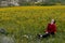 Young woman sitting in the field with yellow marguerite flowers enjoying nature in spring.