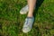 Young woman sitting on green grass in white soiled sneakers. Top view. Long shadows of the setting sun