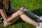 A young woman sitting on a green lawn holds on to a damaged knee. Sprain or cramp Overtrained injured person when training