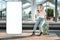 Young woman sitting on her luggage and waiting departure from train station using cellphone. Big smartphone with mock up