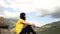 Young woman sitting on hill. Dreamy female sitting on altitude and looking at Peaks of magnificent rocks located against