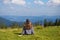 Young woman sitting on mountain top peacefully gazing at low-lying morning clouds