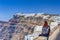 Young Woman Sitting on Parapet in Front of Panoramic View of Thira City in Santorini Island in Greece