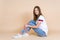 Young woman sitting on pastel beige background, looking at camera