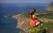 Young woman sitting on a precipice, view from behind. Incredible view of small village on ocean coast