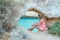 Young woman sitting and relaxing under a natural limestone arch formation by the Algarves, Portugal