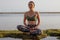 Young woman sitting on the rock in lotus pose, meditating, practicing yoga and pranayama. Deep breath and concentration with