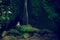 Young woman sitting on the rock, practicing yoga near waterfall. Hands in gyan mudra. Leke Leke waterfall, Bali. View from back