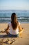 Young woman sitting on the sand in lotus pose in front of the ocean. Yoga at the beach. Hands in gyan mudra. Meditation concept.