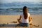 Young woman sitting on the sand in lotus pose in front of the ocean. Yoga at the beach. Hands in gyan mudra. Meditation concept.