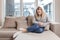 Young woman sitting on sofa holding hands on stomach twisted from pain, poisoned or menstrual pain