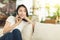 A young woman sitting on the sofa at home holding a phone while talking, leisurely and happily discussing work with colleagues or