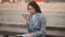 Young Woman sitting on stairs while talking on phone, working with papers documents on laptop in the street.