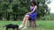 Young woman sitting on the stump with dachshund dog in park and rewritten by smartphone