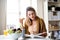 Young woman sitting at the table indoors at home, reading and eating.