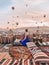 Young woman sitting on the terrace in Cappadocia watching sunrise and air balloons