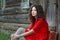 Young woman sitting on threshold of old log cabin with retro suitcase