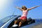 Young woman sitting on top of cabrio sport car in summer vacation with arms open to the air