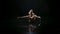 Young woman sitting on water surface in dark studio performs a handstand. Wet slender body glitters in studio light