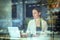 Young woman sitting at window table in cafeteria drinking coffee and working on laptop