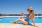 Young woman with slice of watermelon in straw hat sunbathing sitting on the edge of swimming pool