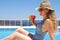 Young woman with slice of watermelon in straw hat sunbathing sitting on the edge of swimming pool