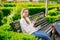 Young woman with smartphone resting on bench in green square